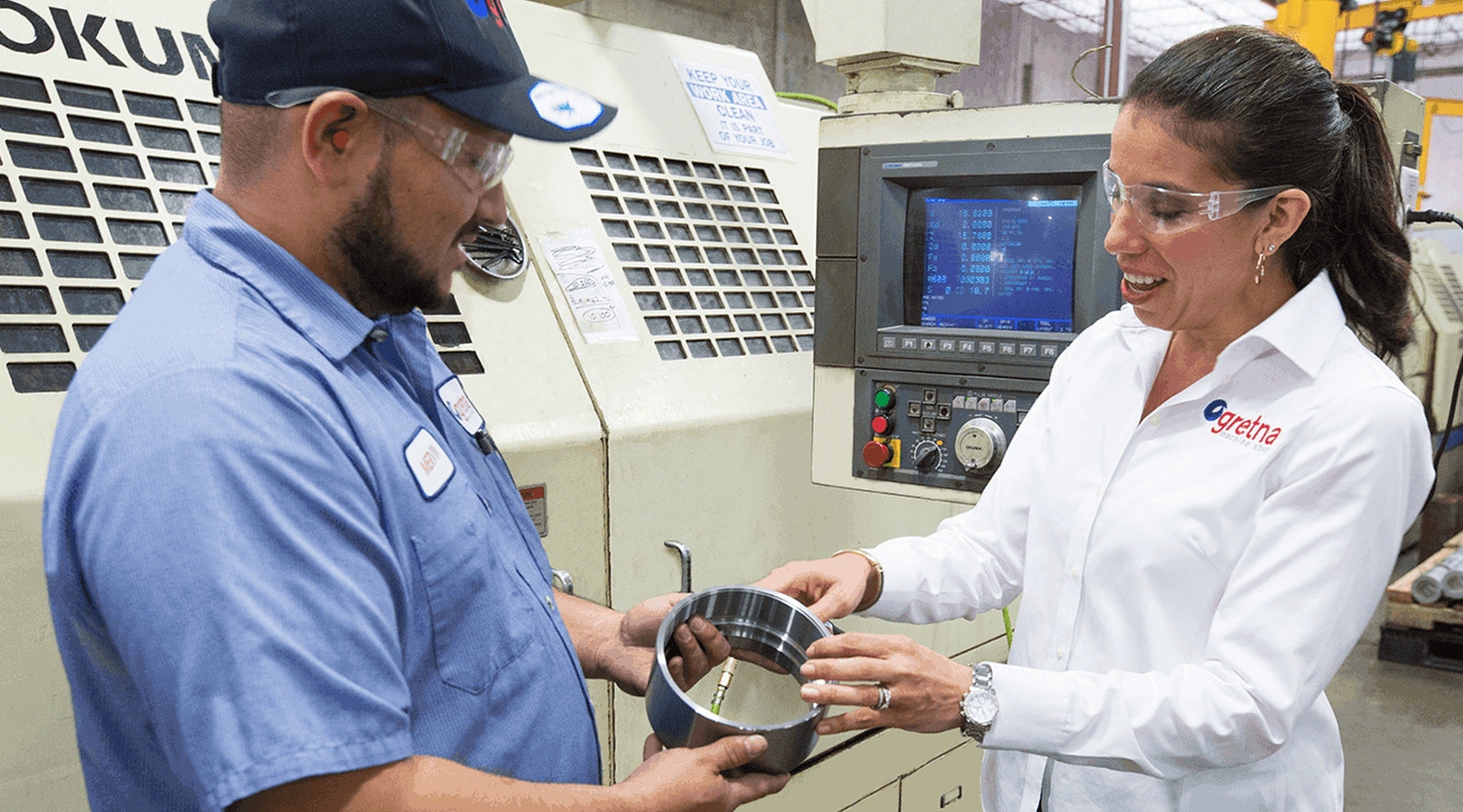 Nubia Perez, CEO of Gretna Machine Shop, inspecting a machined part with a machinist at a CNC lathe
