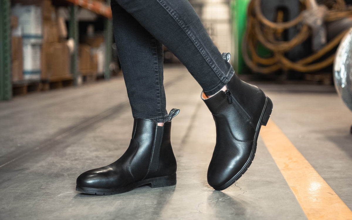 Xena Workwear Omega EH Stylish Black women's steel toe safety boots — lifestyle photo of woman in industrial warehouse setting