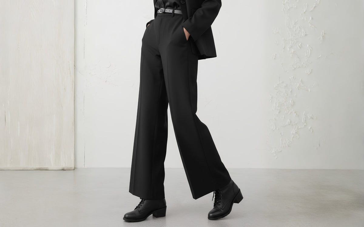 Woman wearing Xena Vega steel-toe safety boots in classic black leather with black wide-leg trousers and blazer, mid-stride in a studio setting